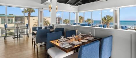 A restaurant with a view of the ocean, large windows, and blue upholstered chairs.