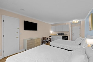 A hotel room with two beds, a TV, a kitchenette, and a dining area.