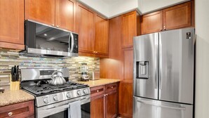 Una cocina con armarios de madera, un refrigerador de acero inoxidable, un microondas, una estufa y un salpicadero de azulejos.
