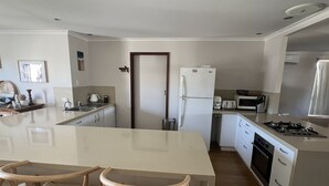 Una cocina moderna con una isla central, sillas de madera, refrigerador, microondas, estufa y un lavaplatos.
