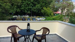 A balcony with two plastic chairs and a table, a lantern, and a view of parked cars and trees. - Apartament Konopnicka (Swinoujscie)