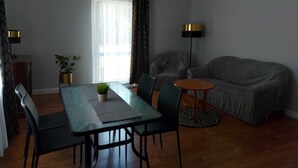 A modern living room with a dining table, two chairs, a grey sofa, a floor lamp, and a potted plant. - Apartament Konopnicka (Swinoujscie)