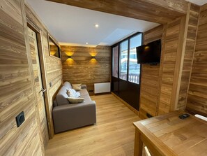 Ein modernes Zimmer mit Holzwänden, einem grauen Sofa, einem Holztisch und einem an der Wand befestigten Fernseher.