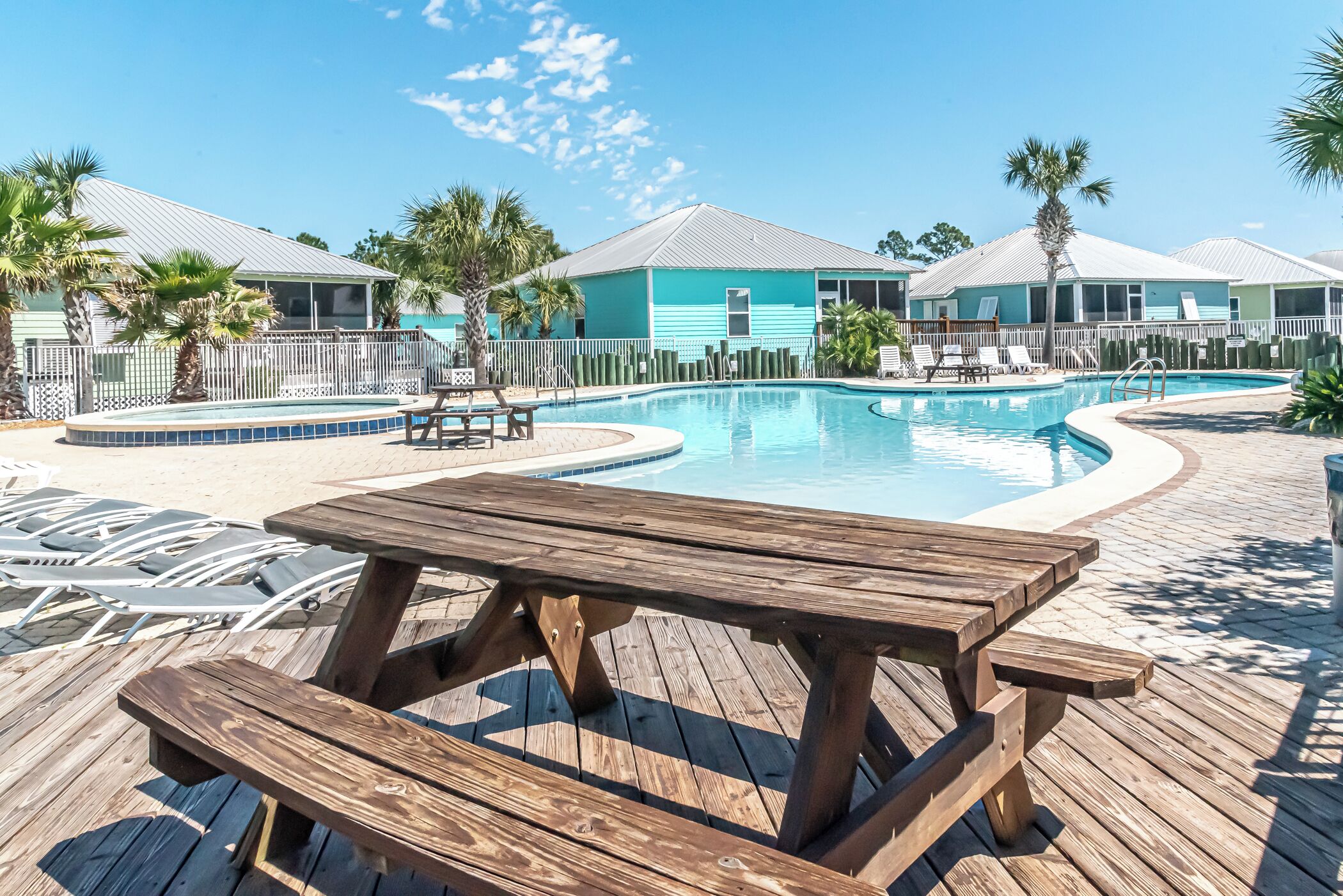 Une terrasse en bois avec une piscine, des chaises longues et une table de pique-nique.