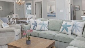 A living room with a light-colored sofa, a wooden coffee table, and a chandelier. - 6015 Rookery 3 Tropic like is hot (Gulf Shores)
