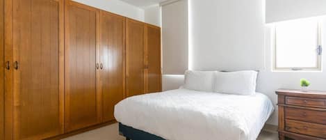 Un dormitorio con cama, armario de madera, ventilador de techo y ventana con persianas.