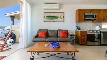 A living room with a sofa, a coffee table, and a kitchen area with a microwave and oven.