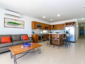 Una cucina moderna con mobili in legno, un'isola centrale con sgabelli e un'area pranzo con divano e tavolino.