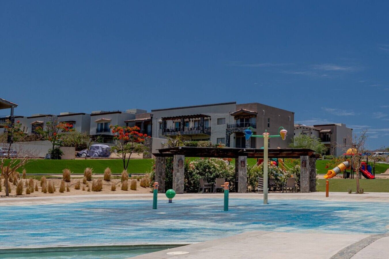 A pool area with a water slide, a covered seating area, and modern buildings in the background.