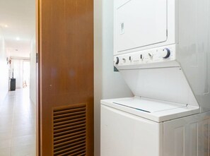 Un área de lavandería con una lavadora y secadora blancas, una puerta de madera y piso de baldosas.
