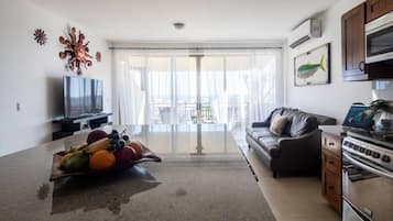 A modern living room with a flat-screen TV, a fruit bowl, a sofa, and a kitchen area with an oven.