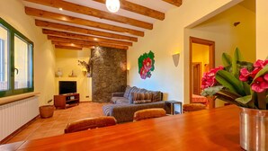 Amplia sala de estar con chimenea de piedra, vigas de madera, un sofá y una mesa de comedor.