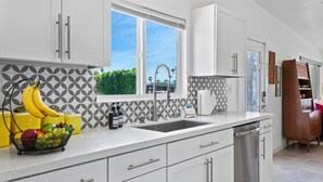 A modern kitchen with white cabinets, a stainless steel sink, and a window with a view of greenery. - Beautiful home in the highly desirable Tahquitz Estates neighborhood. (Palm Springs)
