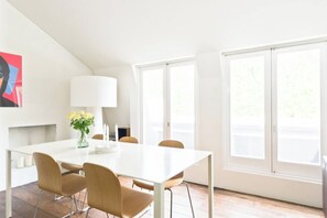 A modern dining area with a white table, four chairs, a vase with flowers, and a lamp.