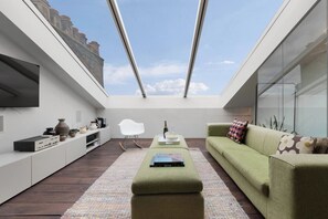 A modern living room with a high ceiling, a green sofa, a white chair, and a flat-screen TV.