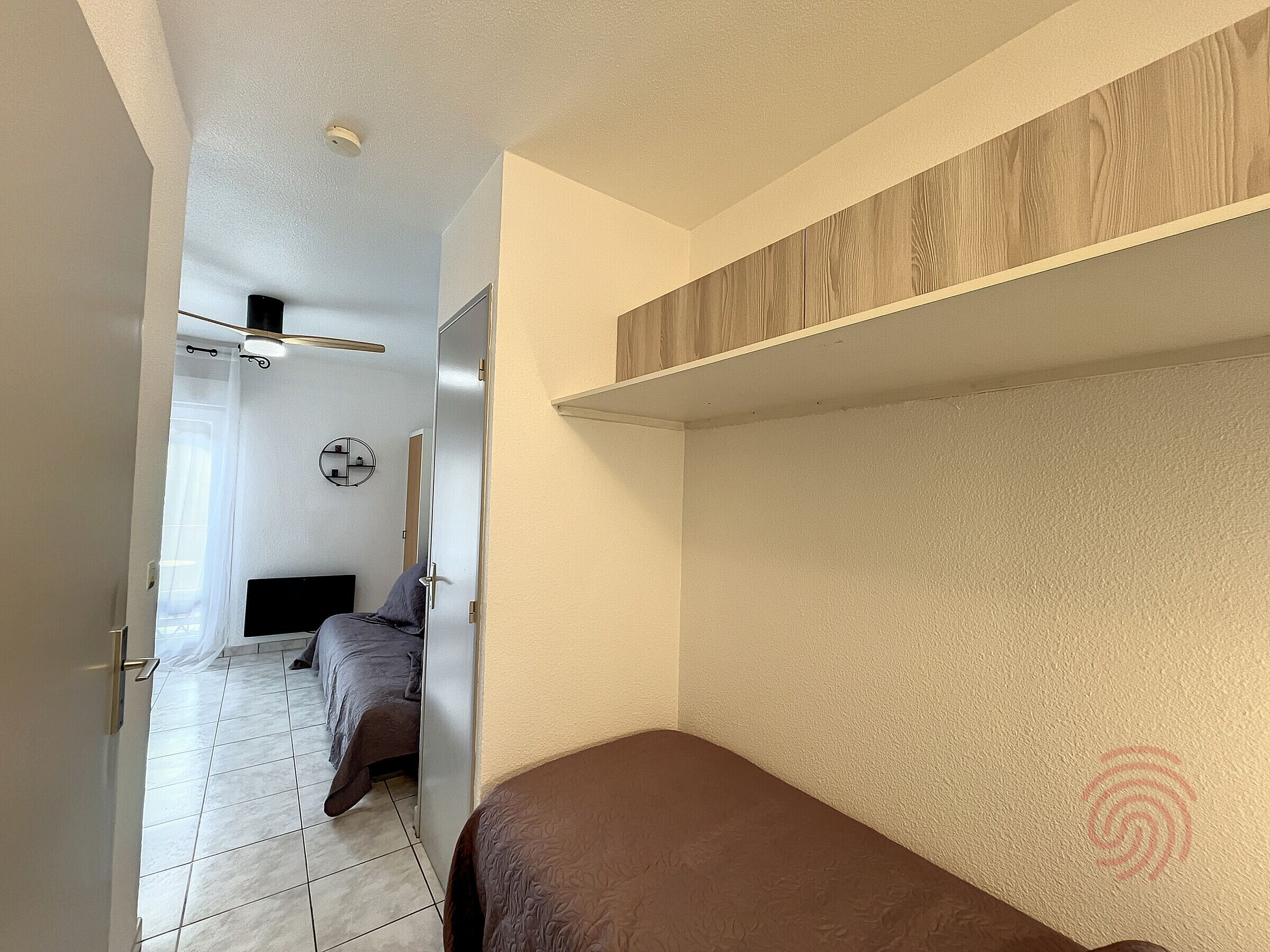 A compact room with a bed, a small desk, and a mirror on the wall.