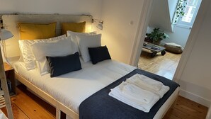 A bed with white bedding, multiple pillows, a dark blue throw blanket, and a bedside lamp. - Cozy Apartment, Refurbished but Keeping the Ancient Style of old Lisbon (Lisboa)