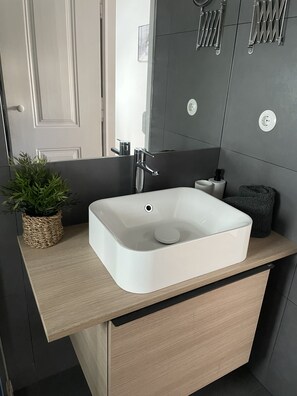 Une salle de bain moderne avec un lavabo blanc, un plan de toilette en bois et des murs recouverts de carreaux foncés.