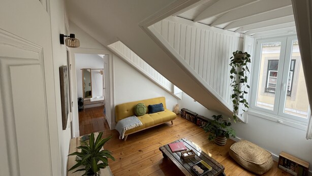 A spacious living room with a wooden floor, a yellow sofa, a coffee table, and a staircase with a skylight. - Cozy Apartment, Refurbished but Keeping the Ancient Style of old Lisbon (Lisboa)