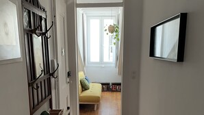 A hallway with wooden flooring, a white door, a coat rack, and a television mounted on the wall. - Cozy Apartment, Refurbished but Keeping the Ancient Style of old Lisbon (Lisboa)