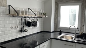 A modern kitchen with white cabinetry, a black countertop, and a window providing natural light. - Cozy Apartment, Refurbished but Keeping the Ancient Style of old Lisbon (Lisboa)
