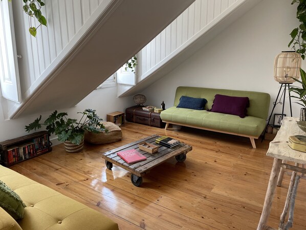 Un salon chaleureux, aménagé dans un style industriel, avec un canapé vert, un plancher en bois et une variété de livres et d’objets décoratifs.