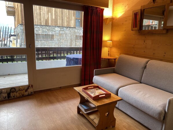 Une pièce chaleureuse avec un canapé, une petite table en bois sur laquelle est posé un plateau, une lampe et une vue sur une clôture en bois à l’extérieur.