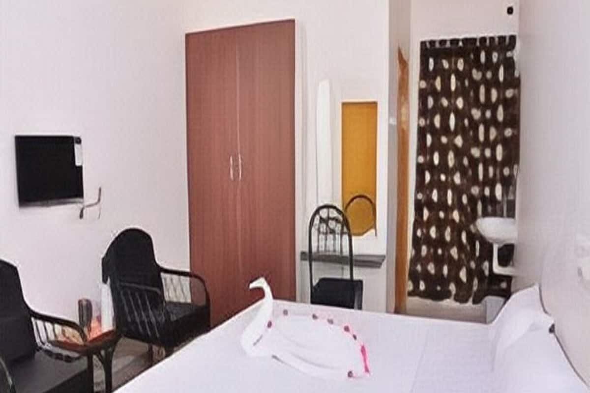 Habitación de hotel con cama, escritorio, silla, armario y televisor en la pared.