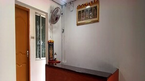 Un espace d’accueil avec un comptoir en bois, un ventilateur et une icône religieuse encadrée accrochée au mur.