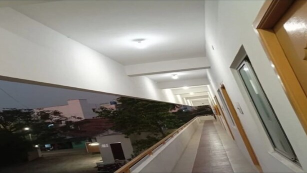 Un couloir avec une porte en bois et des fenêtres, qui mène à un balcon offrant une vue sur l’extérieur.