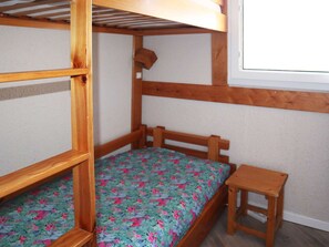 Una cama litera con estructura de madera, una mesita de madera pequeña y un ventanal con marco blanco.
