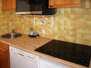 Una cocina con lavavajillas, placa de inducción, microondas y un colgador para ollas.