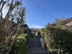 Un escalier menant à un bâtiment dont le toit est recouvert de tuiles, le tout étant entouré de verdure.