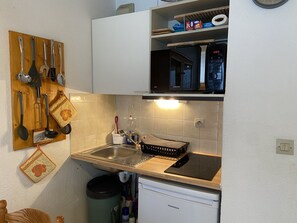 Una cocina compacta con un lavamanos, estufa y varios utensilios colgados en una tabla de madera.