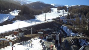 A ski resort with a chairlift, buildings, and a snowy mountain backdrop.