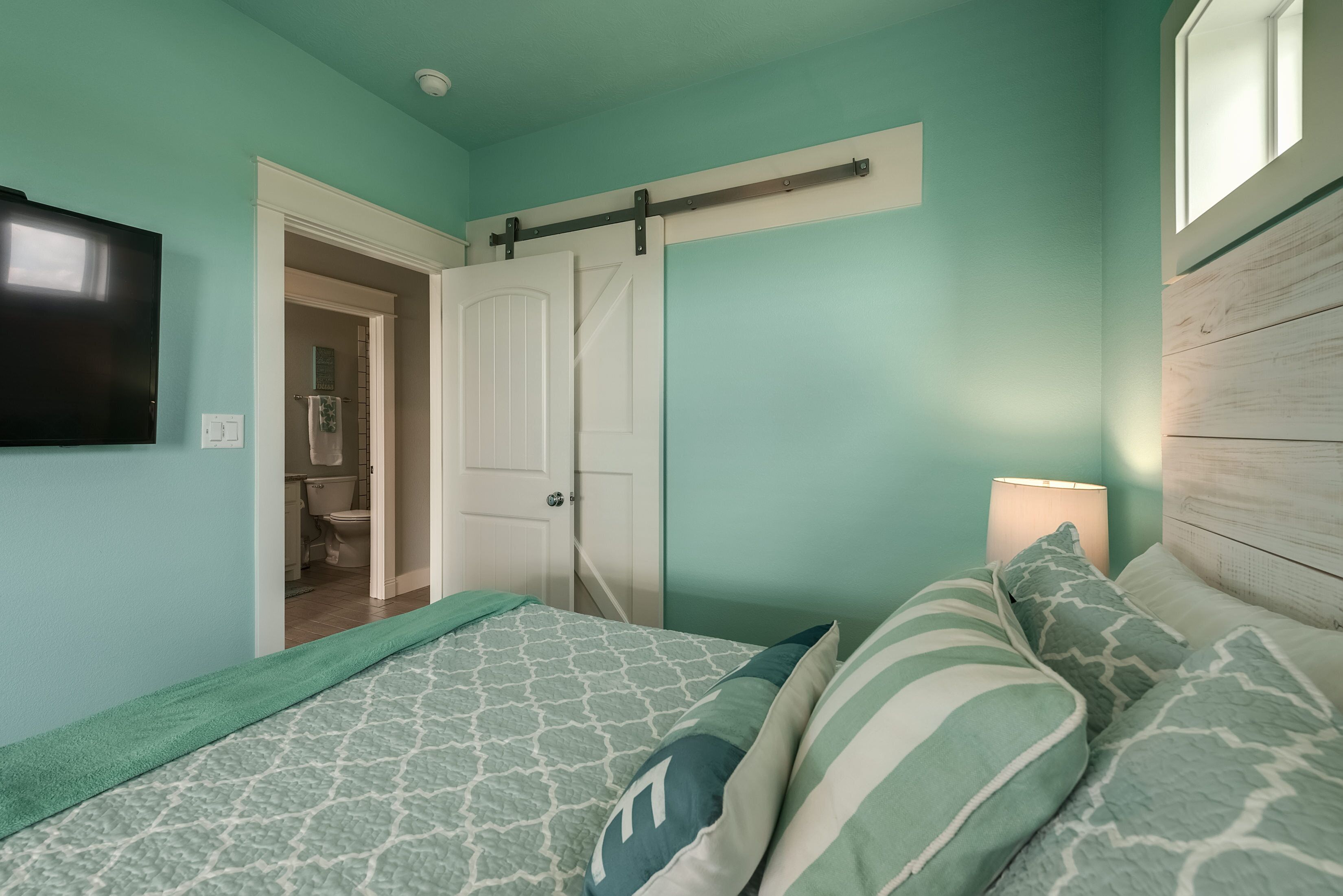 A bedroom with a bed, pillows, a TV, a sliding door, and a nightstand with a lamp.