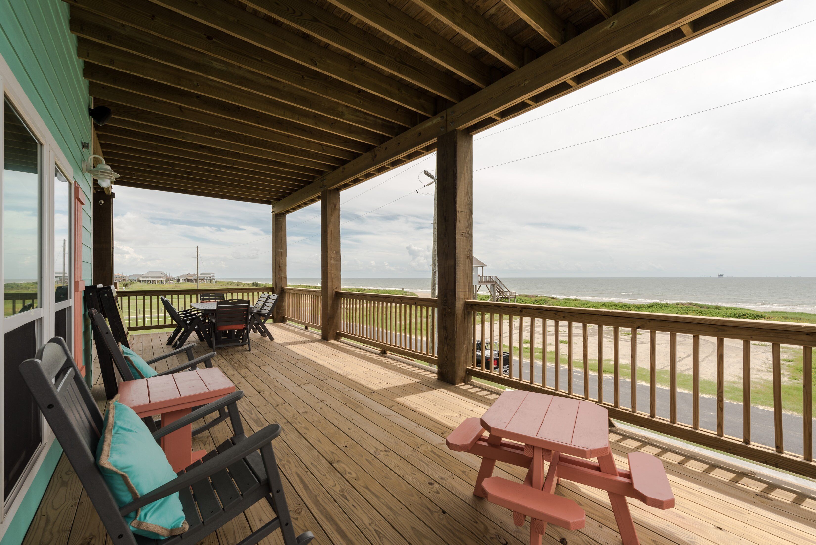 A covered deck with wooden furniture and a view of the beach.