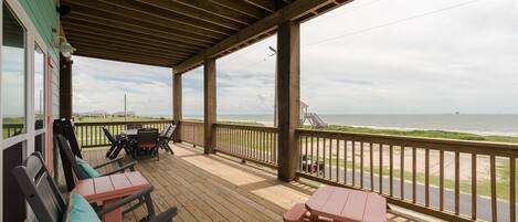 A covered deck with wooden furniture and a view of the beach.