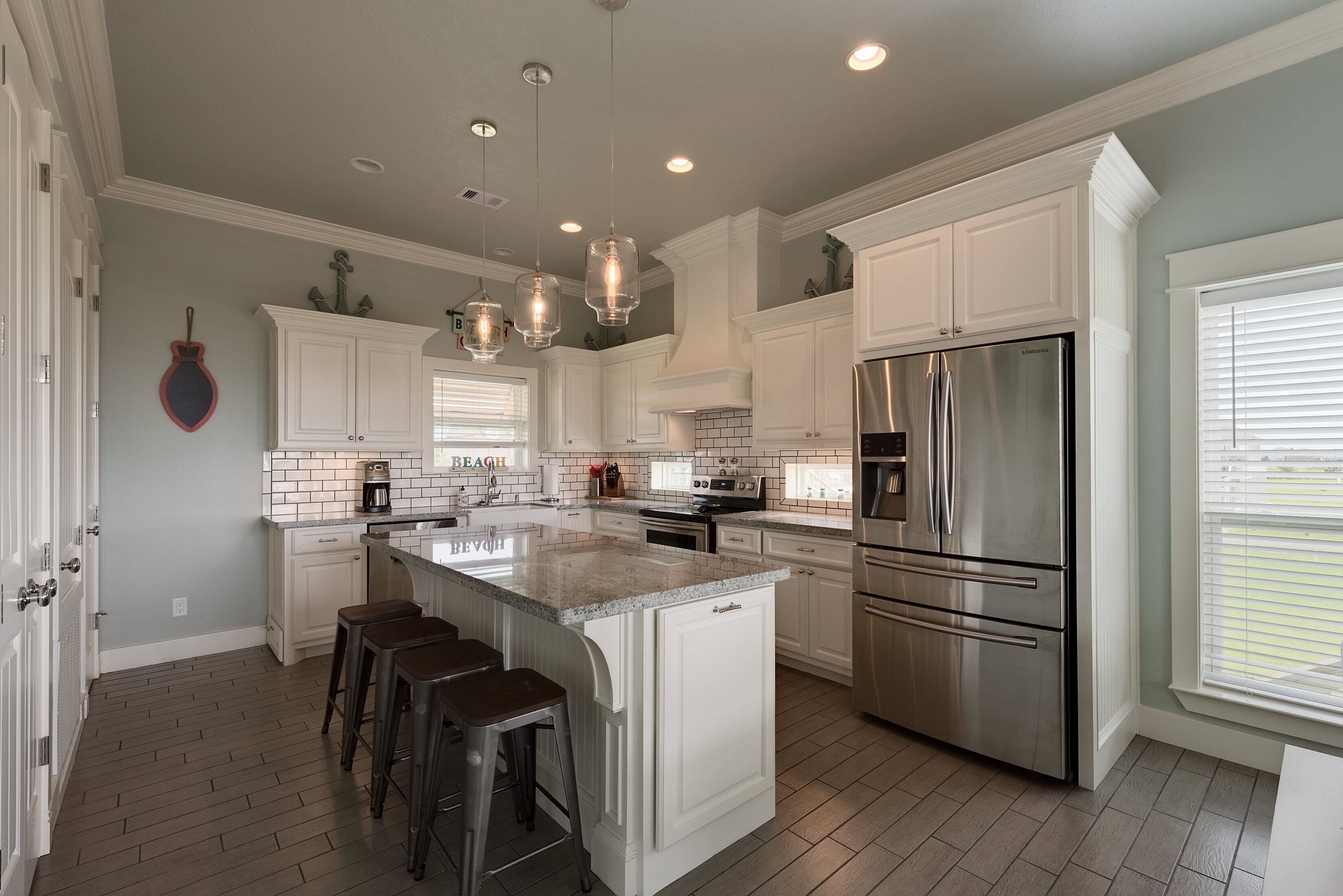 A modern kitchen with white cabinetry, a stainless steel refrigerator, and pendant lighting.