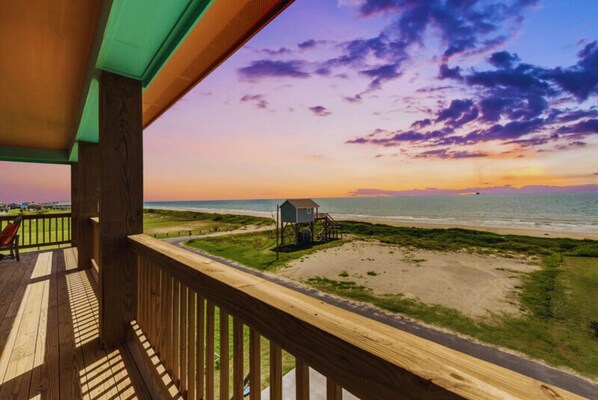 A wooden deck overlooking a beach with a small structure on the sand.