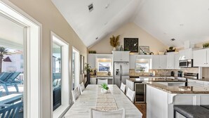 Una cocina amplia con muebles blancos, una isla central y un comedor con una mesa larga y sillas.