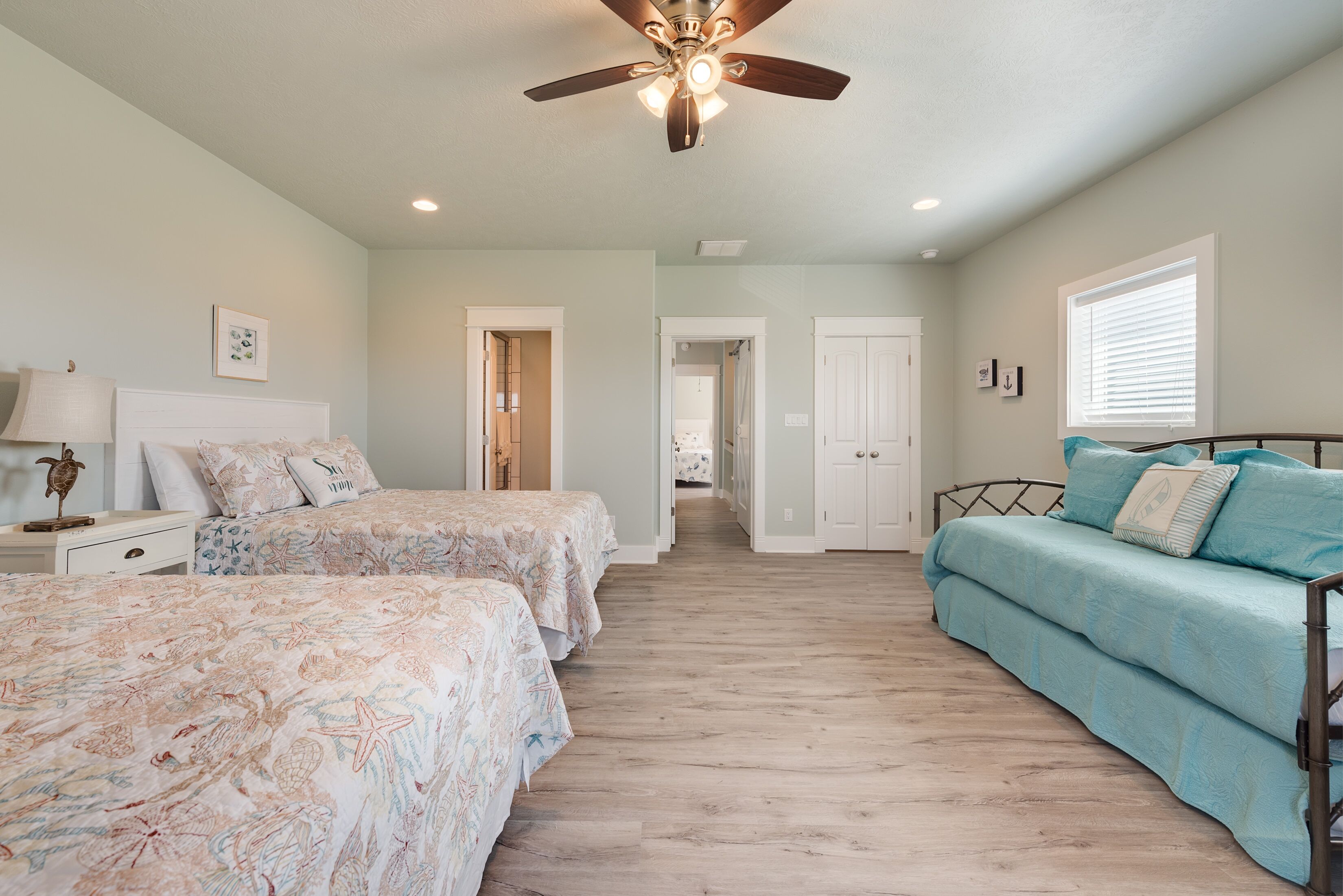 A bedroom with two beds, a ceiling fan, and a window with blinds.