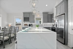 A modern kitchen with a large island, stainless steel appliances, and a dining area with wooden chairs and a table.
