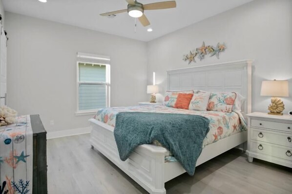 A bedroom with a bed, nightstands, a ceiling fan, a window, and a decorative wall piece.