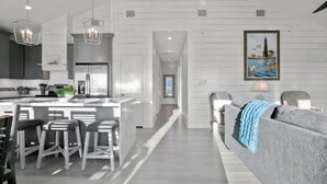 A modern kitchen with a central island, bar stools, and pendant lighting. - Gulf Views | Modern Amenities, Deck, Sleeps 12 & More (Port Bolivar)