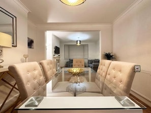 A dining area with a glass-top table, four upholstered chairs, and a central decorative bowl.