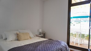 Ein Schlafzimmer mit Bett, Nachttisch, Lampe und Blick auf eine Außenpatio mit Stühlen und Sonnenschirmen.