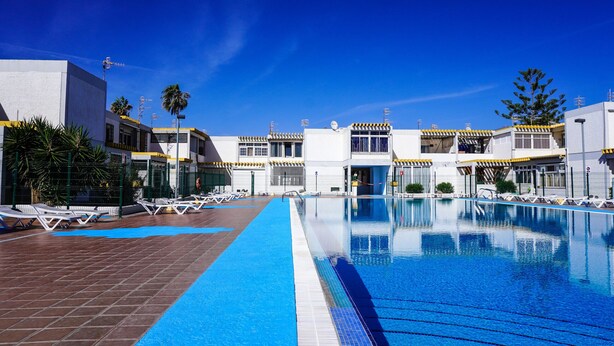 Ein Schwimmbecken mit Liegestühlen und ein Gebäude mit einem Ziegeldach.