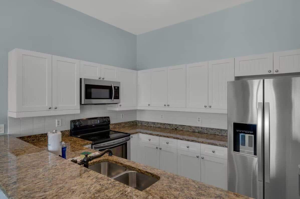 Una cocina con gabinetes blancos, un refrigerador de acero inoxidable, un microondas y una encimera de granito.