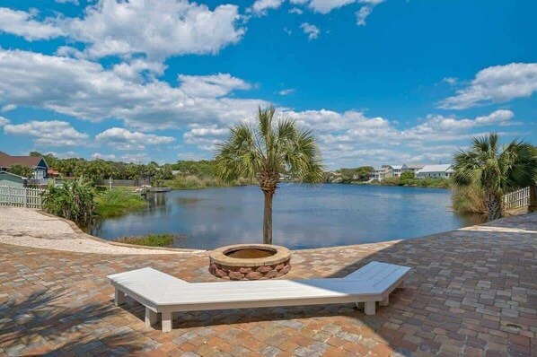 A poolside area with a lounge chair, a fire pit, and a view of a lake.
